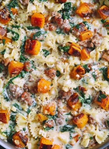 Creamy butternut squash pasta dish with sausage and spinach garnished with herbs.