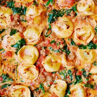 Creamy tortellini with sausage, spinach, tomatoes, and mozzarella in a bowl.