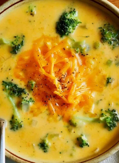 Bowl of creamy broccoli cheddar soup with fresh broccoli and cheese on top